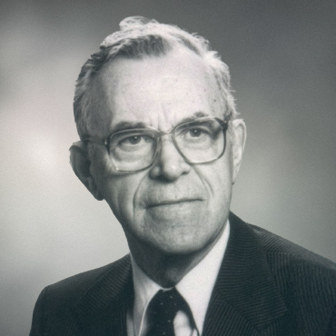 A black and white portrait of Moses Osbourne Morgan. The background is blurred. He is wearing a suit and a tie and is smiling.