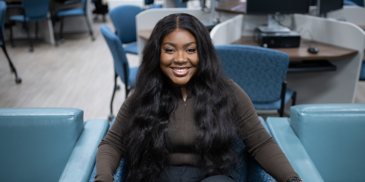 Nicole Obiodiaka seated in a common area at Memorial University looking up and smiling