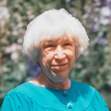 A colorful portrait of Violetta Halpert. Background has a lot of trees. The photo was taken during the daytime. She is wearing a light blue dress, and smiling.