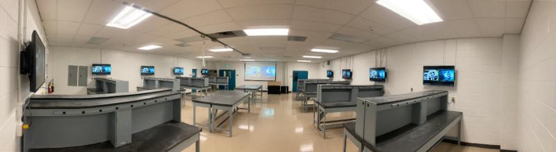 wide photo of an engineering lab with multiple monitors on the walls; empty tables; no equipment