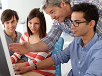 An instructor pointing at a computer screen while students look on