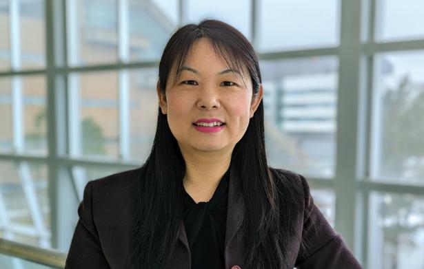 A woman with black hair and a black shirt smiles in front of a window