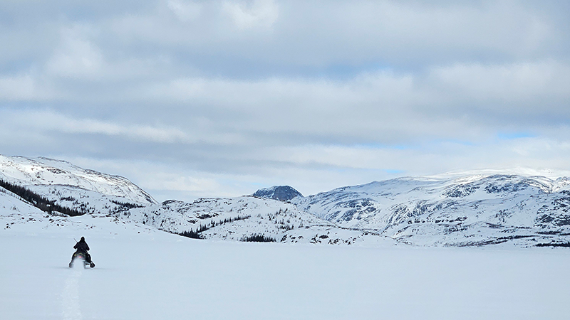 A person in silhouette walking on a glacier with mountains and clouds in the background