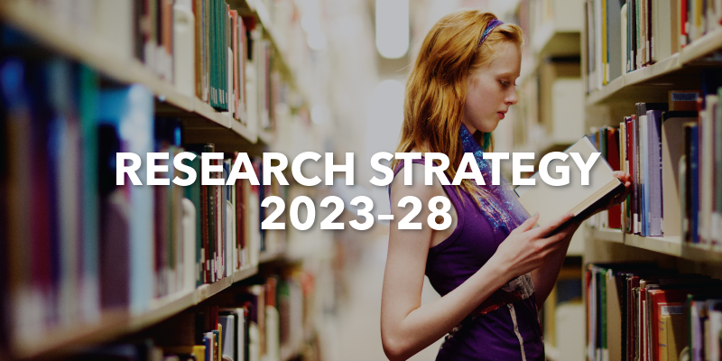 A photo of a woman holding a book pictured in a library with the text Research Strategy 2023-28