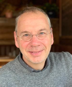 Dr. Ray Gosine is seen smiling wearing glasses and a grey sweater.